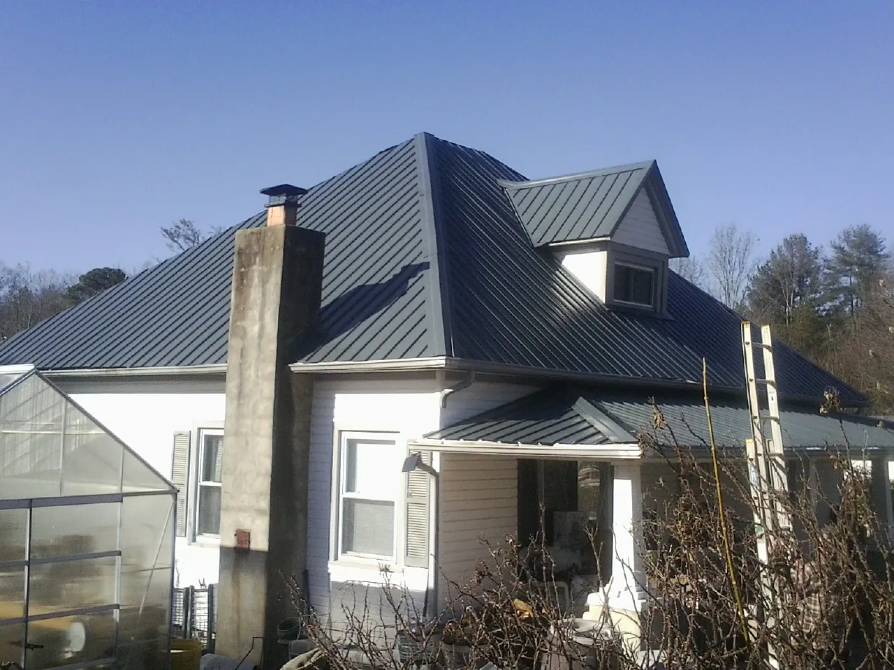 Dark blue standing seam metal roof on a white farmhouse with dormer — Slate & Tile Roof Repair by Roofing Brothers in Etoile
