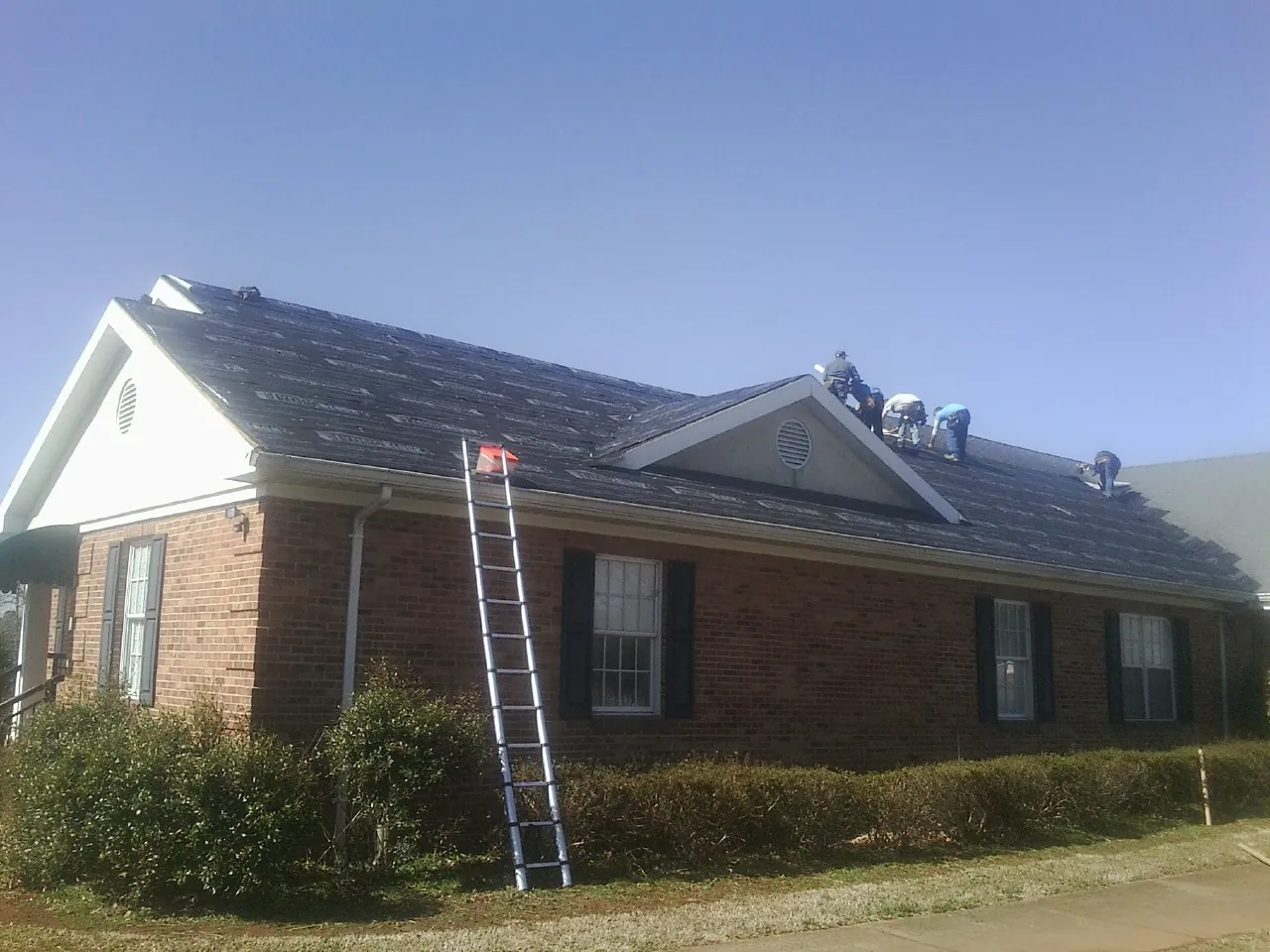 Crew tearing shingles off a brick ranch roof with a ladder set — Metal Roof Repair work by our crew in Etoile