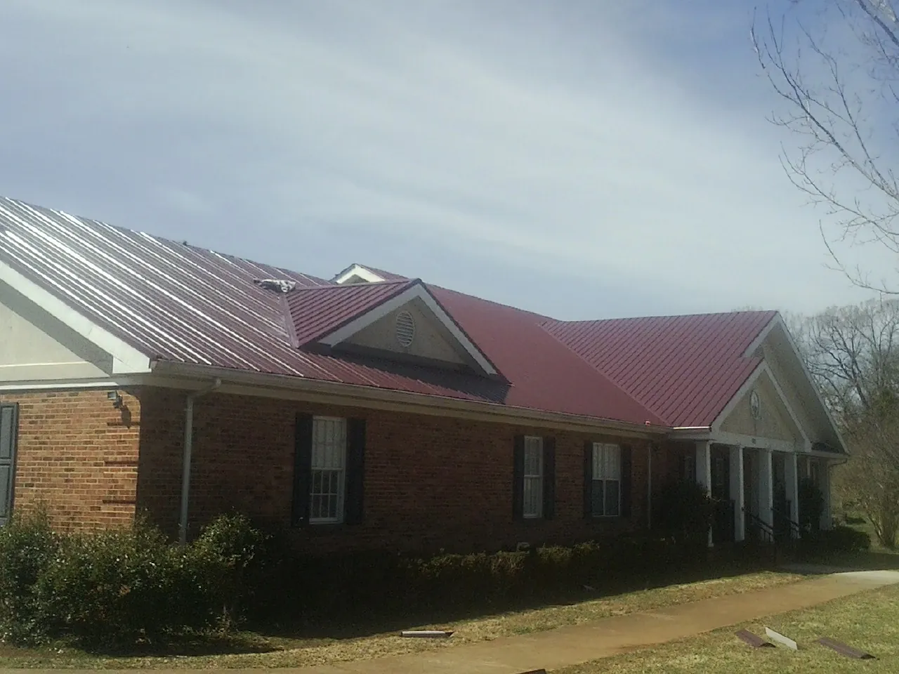 Red metal roof with gabled entries on a long brick building, from a Hail Damage Roof Repair job in Etoile