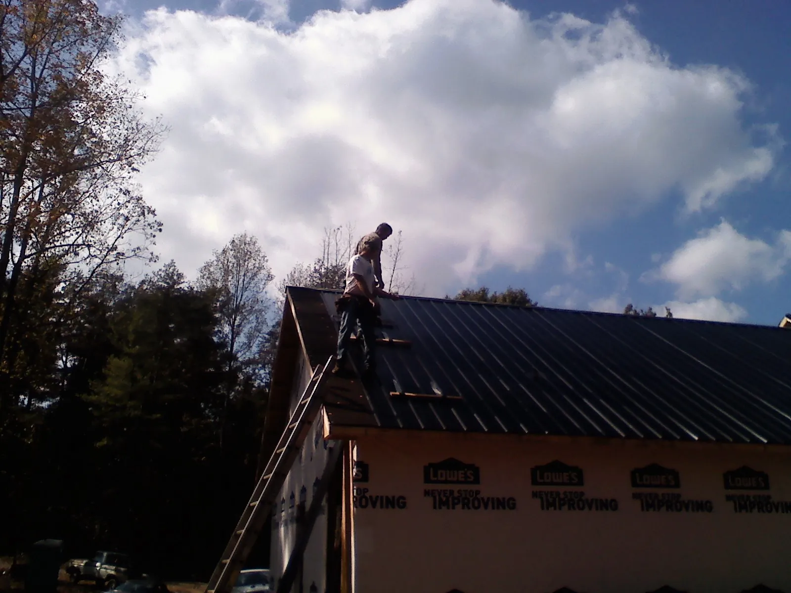 Roofer fastening dark metal panels high against a cloudy sky, from a Roof Inspection job in Etoile