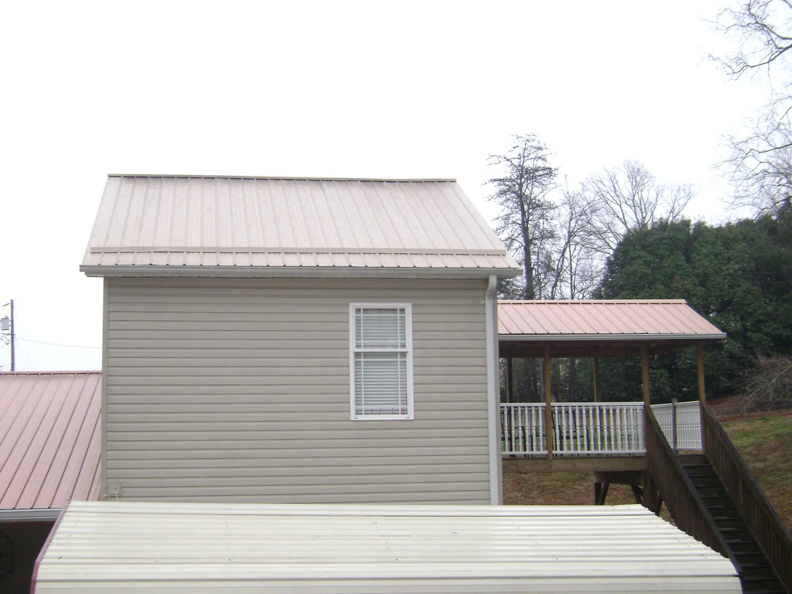 Tan metal roofs on a two story addition and attached porch, from a Roof Replacement job in Etoile